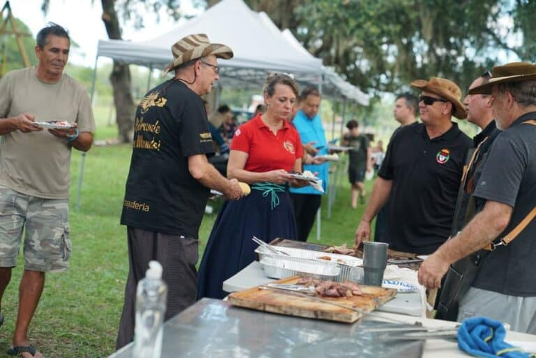 Pessoas servindo e recebendo comida em uma confraternização ao ar livre sob tendas