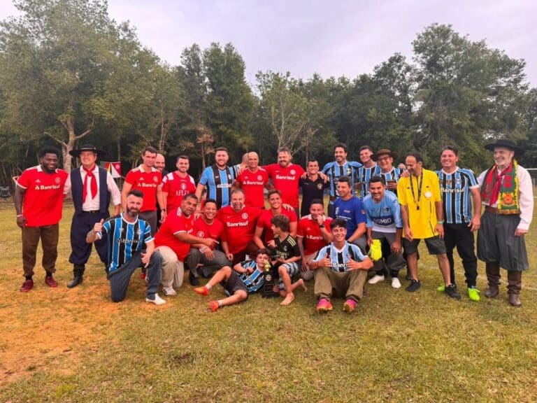 Grupo de homens posando em campo gramado, muitos com camisas do Grêmio e do Internacional, em clima de confraternização