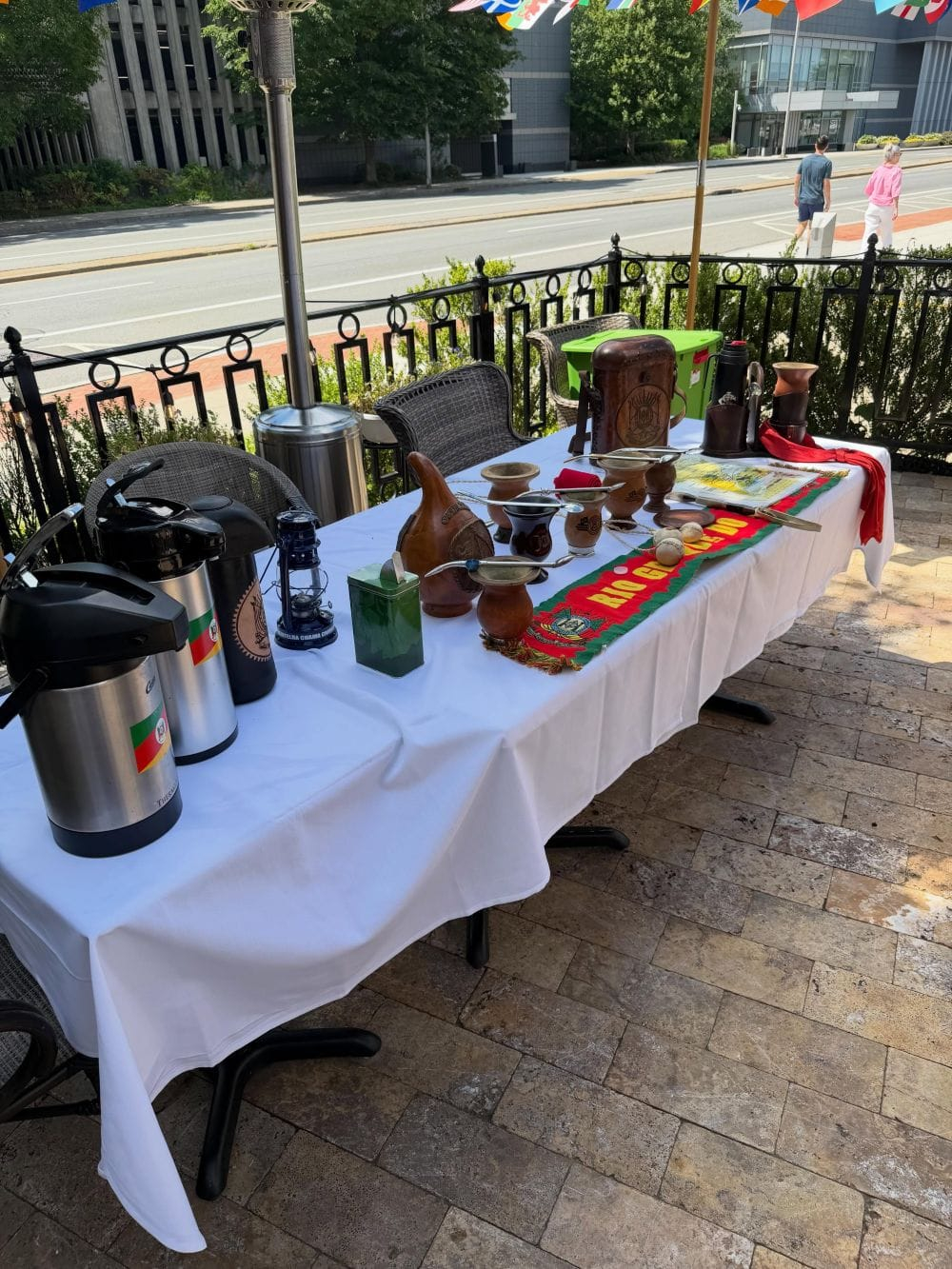 Mesa com cuias, térmicas e utensílios de chimarrão ao ar livre, ao lado de uma rua