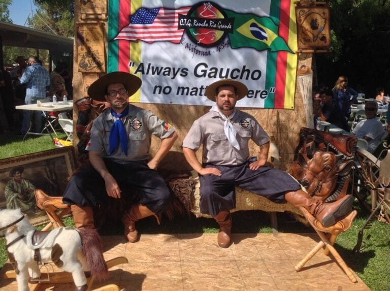Dois homens vestidos de gaúchos posam diante de uma faixa com as bandeiras dos EUA e do Brasil