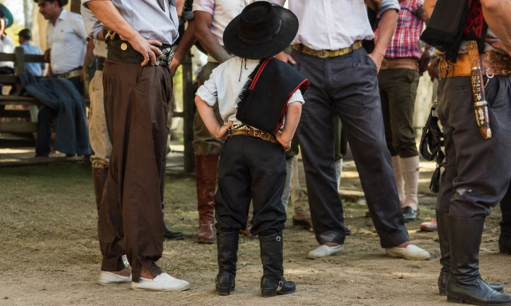 Criança vestida com traje tradicional entre adultos em um evento ao ar livre