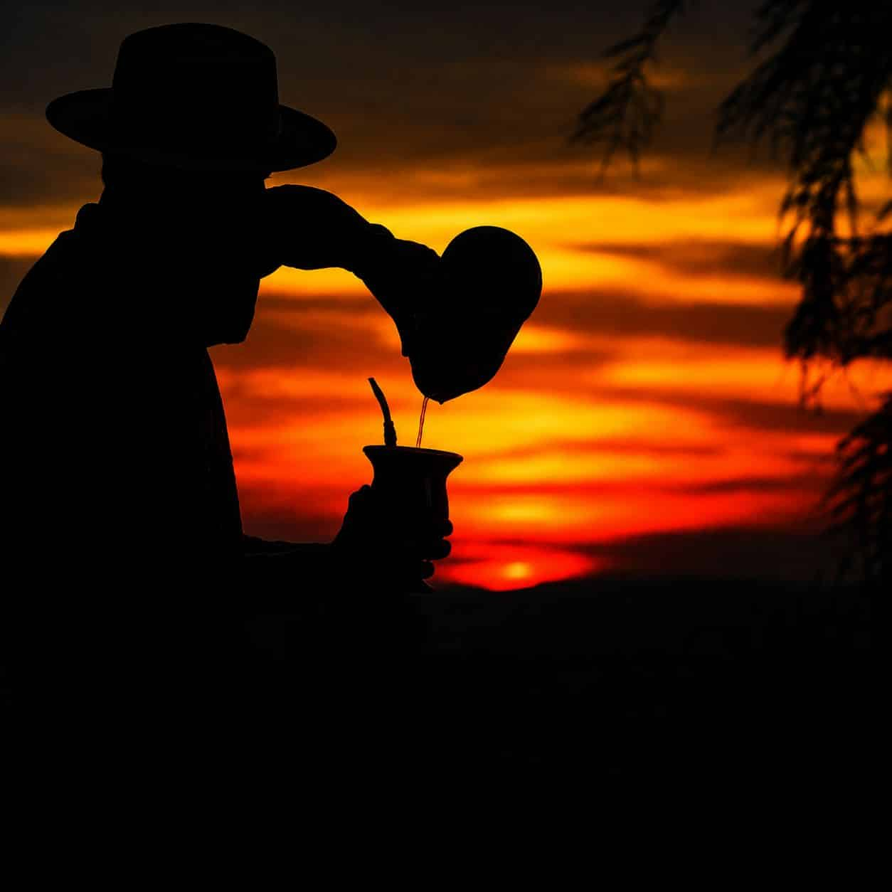 Silhueta de gaúcho preparando chimarrão ao pôr do sol