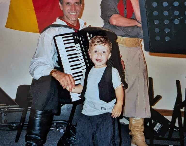 Menino pequeno em frente a um homem com acordeão, em um ambiente de apresentação musical