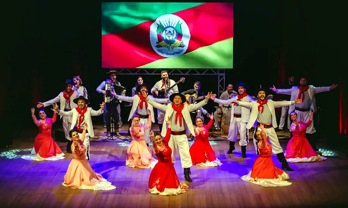 Grupo de Danças Folclóricas Arte Nativa em apresentação no palco com bandeira do Rio Grande do Sul