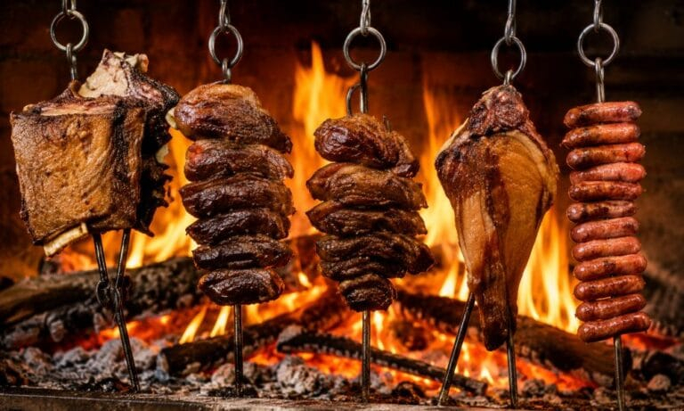 Carnes e linguiças assando em espetos sobre fogo aberto