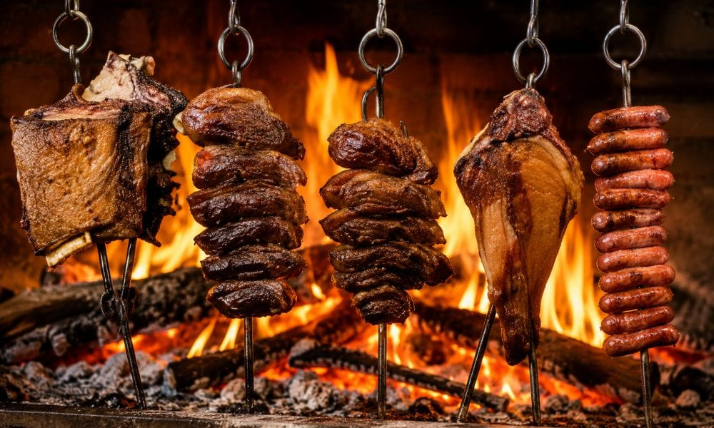 Carnes e linguiças assando em espetos sobre fogo aberto