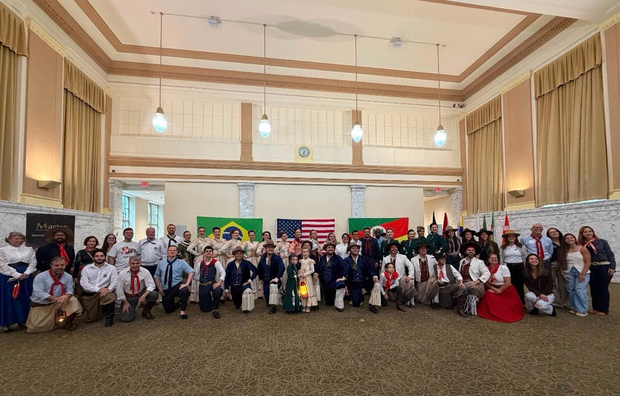 Participantes reunidos em um salão com bandeiras do Brasil, dos Estados Unidos e do Rio Grande do Sul no evento de 19 de setembro de 2026.