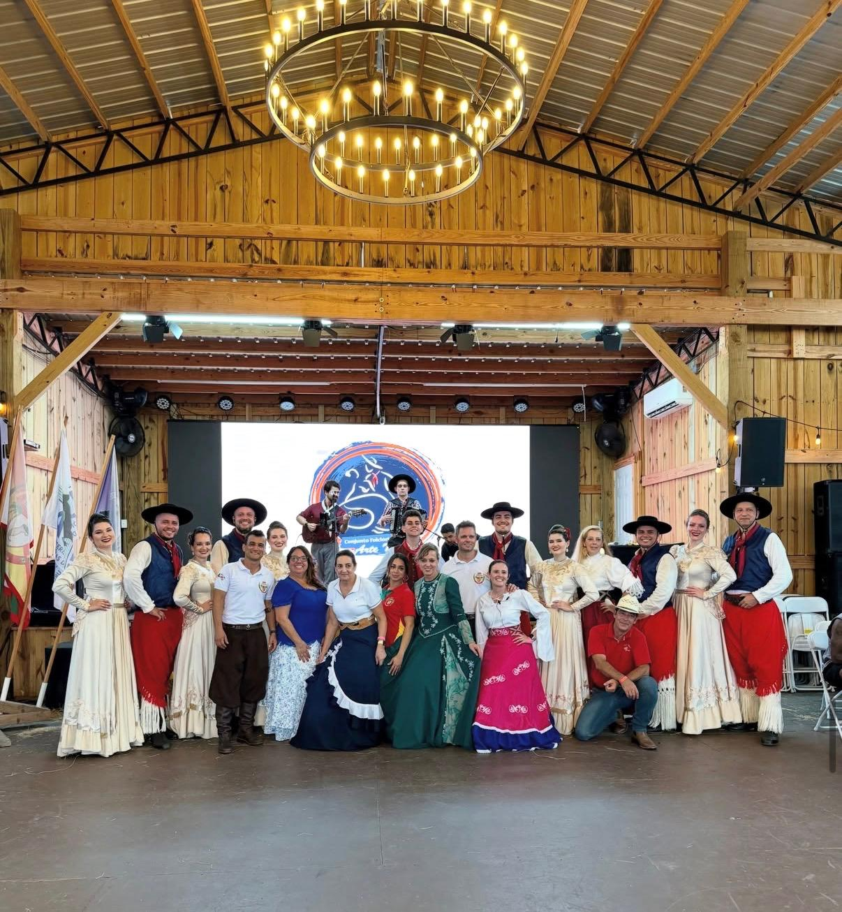 Grupo reunido em frente ao palco, com participantes em trajes tradicionais gaúchos, no evento de 12 de setembro de 2026 em Orlando.