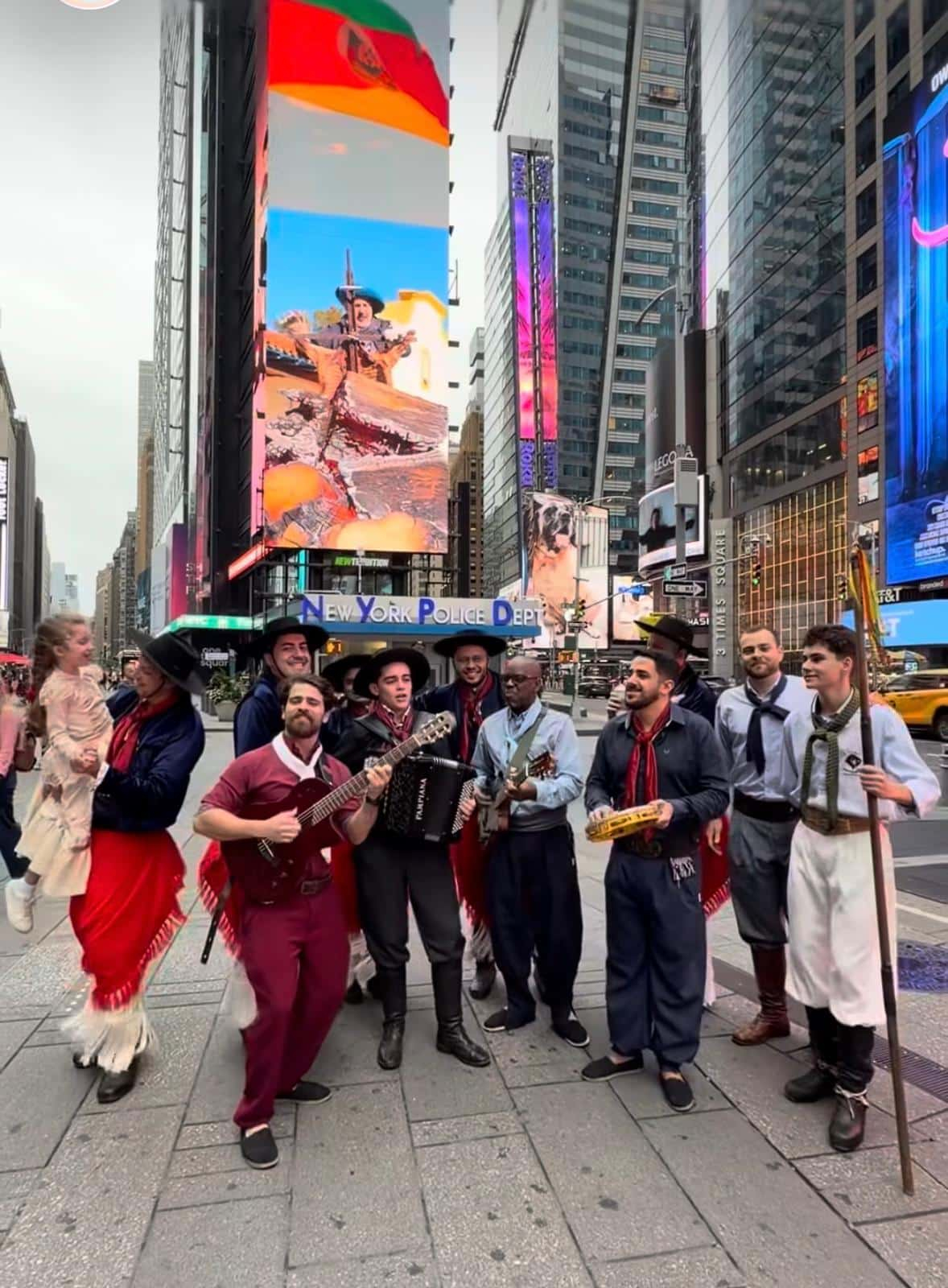 Músicos e participantes em trajes gaúchos na Times Square, com imagens do Rio Grande do Sul no telão.