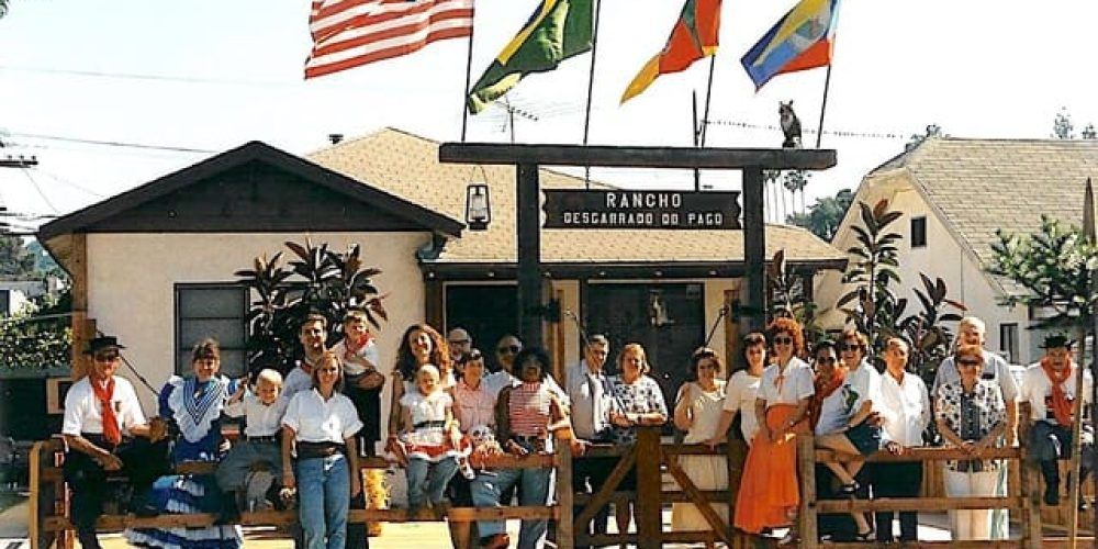 Grupo de pessoas posando em frente ao Rancho Desgarrado do Pago, com várias bandeiras hasteadas acima